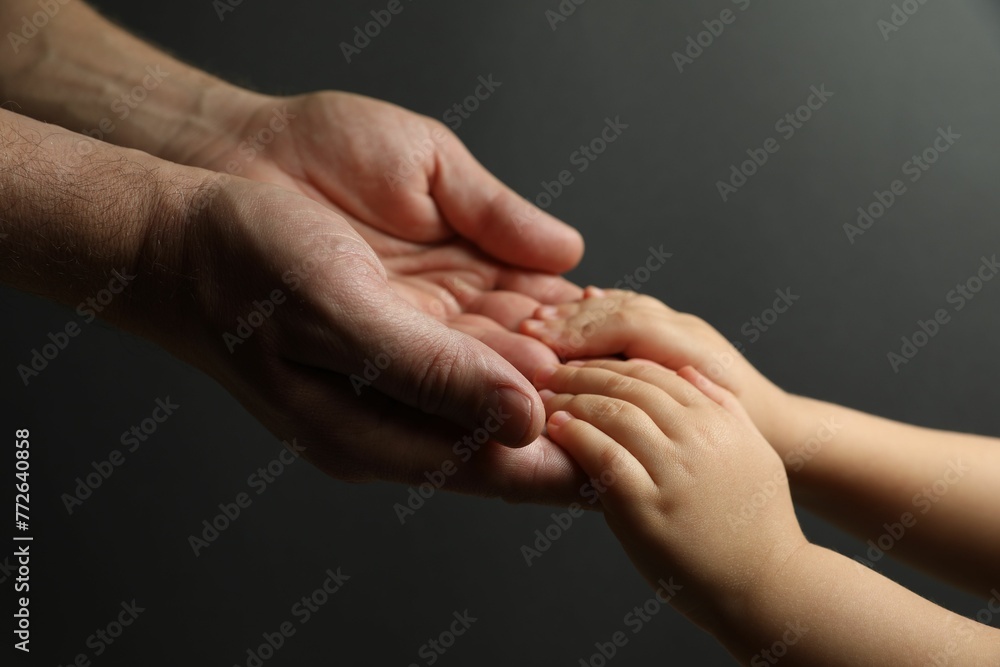 Father and child holding hands on dark grey background, closeup