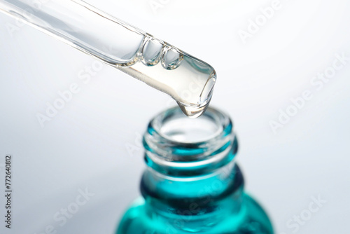 Dripping moisturizing serum from pipette into bottle on light grey background, closeup