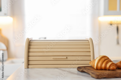 Wooden bread box and board with croissants on white marble table in kitchen