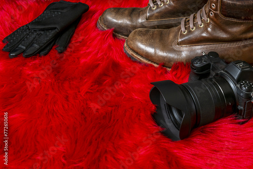 Mirrorless camera with lens hood along with brown leather boots and black gloves on a red furry surface