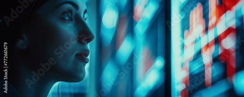 Close-up of a woman's face illuminated by the glow of vibrant data analysis screens, reflecting a digital information era.