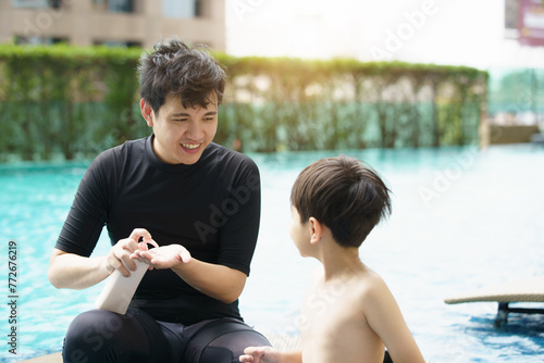 Father is applying a sun screen or sun block lotion on his son body before going to swimming in the swimming pool. photo
