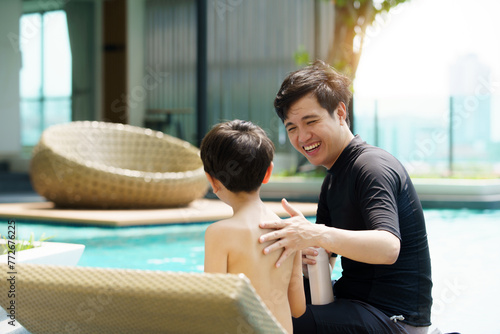 Father is applying a sun screen or sun block lotion on his son body before going to swimming in the swimming pool. photo