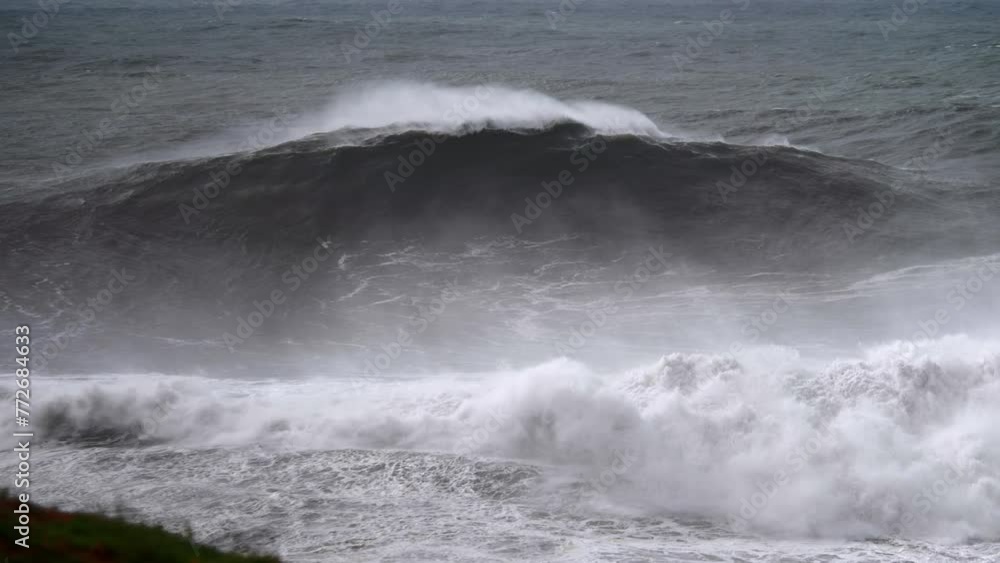Huge big wave breaking in Nazaré, view from the beach with spray in the foreground. Huge big wave breaking in Nazaré, view from the beach with spray in the foreground.