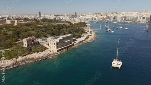 An aerial view of Maneol Island in Marsamxett Harbour, Malta. Taken at on a sunny morning with the resort town of Sliema in the background. Flying left to right around the island photo