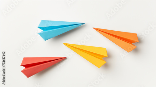 Three colorful paper airplanes on a white surface, in blue, orange, and yellow.