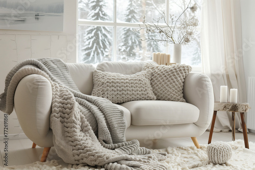 Scandinavian, hygge interior design of modern living room, home. Cozy sofa with pillows and knitted throw against window