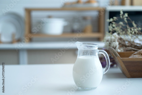 Pitcher of milk prepared for breakfast is placed near a basket of baked bread in the home kitchen, selective focus