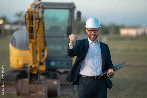 Buider man in suit and hardhat. Construction investor. Business man investor in front of construction site. Successful investor. Handsome man in suit and hardhat at building construction.