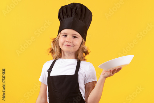 Cute kid boy cook with cooking plate. Child chef cook, studio portrait. Kids cooking. Teen boy with apron and chef hat.