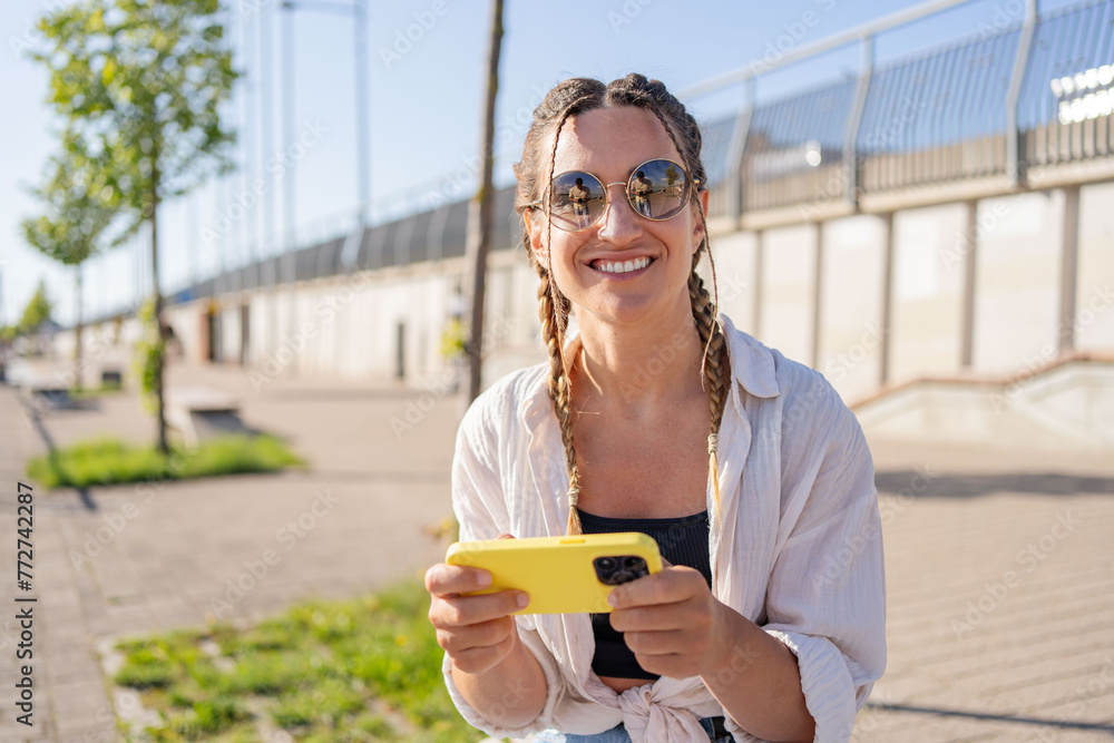 Positive hipster girl holds mobile phone, looks at cellphone screen, uses smartphone apps. girl with mobile phone on the street. Positive hipster girl holds mobile phone, looks at cellphone screen, uses smartphone apps. girl with mobile phone on the street.