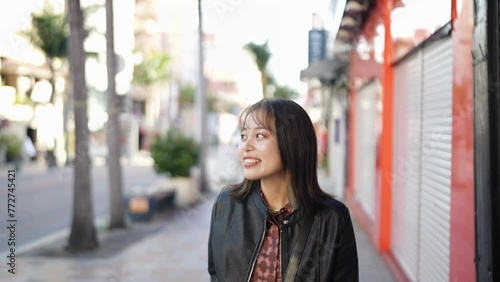 Slow-motion video of an Okinawan woman in her 20s in winter clothes walking on Kokusai Street in Naha City, Okinawa Prefecture with a smile 沖縄県那覇市の国際通りを笑顔で歩く冬服の20代の沖縄県民女性のスローモーション映像 photo