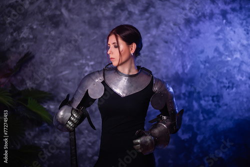 Portrait of a young woman with scars on her face, dressed in black clothes with steel knightly hands and a gorget, holding a bastard sword, posing against an abstract background. Medieval fantasy girl