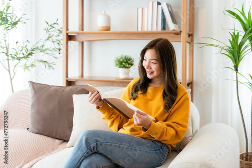 Young beautiful Asian woman reading a book on couch at home