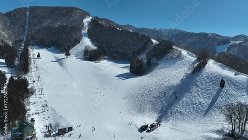 Pull away and orbiting shot of bottom of ski run, skiers arriving at base of mountain lining up for the chairlifts.  Japan Ski Snow Run, Hakuba and Myoko region photo