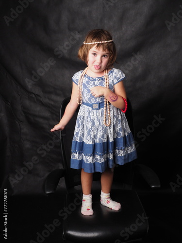 little girl in a blue dress and jewelry on a black background in the studio in full growth (ID: 772761073)
