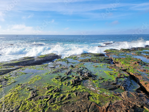 Low tide and the rock platform near Newcastle Ocean Baths, New South Wales, Australia. Green algae on the rocks, with surf crashing over the rocks.