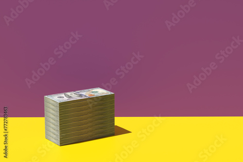 Stack of US 100 dollar bill paper currency on yellow purple background.