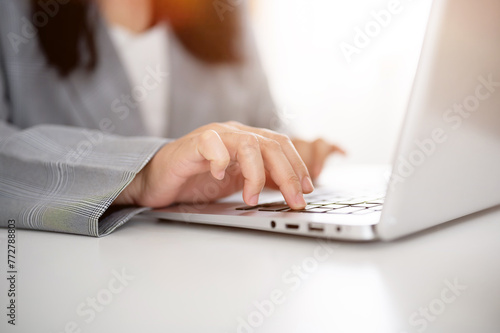 A cropped image of a businesswoman working or browsing on the laptop, working in a modern office.