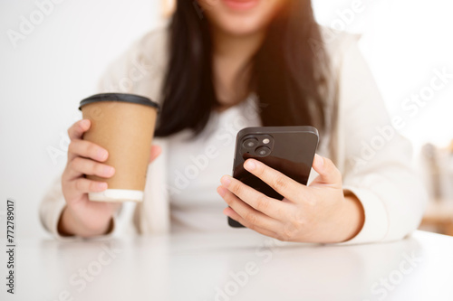 A young Asian woman enjoying a coffee in a cafe while reading messages on her smartphone.