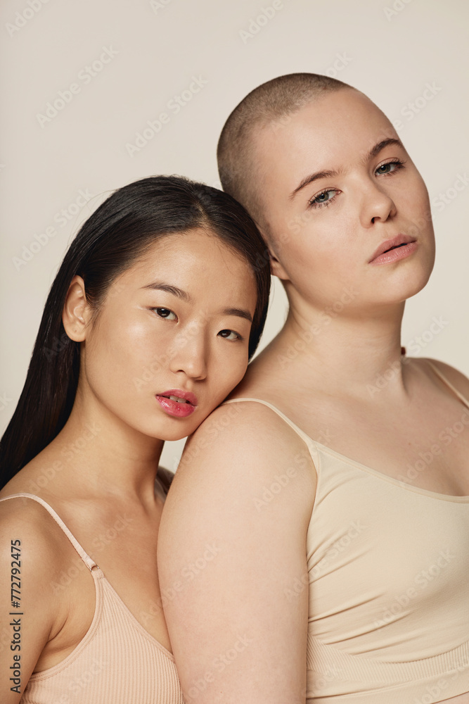Vertical studio portrait of modern young adult Asian and Caucasian women wearing neutral toned underwear posing for camera Vertical studio portrait of modern young adult Asian and Caucasian women wearing neutral toned underwear posing for camera