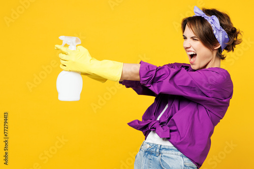 Side profile view excited young woman wears purple shirt rubber gloves do housework tidy up hold in hand use spray bottle isolated on plain yellow background studio portrait. Housekeeping concept.