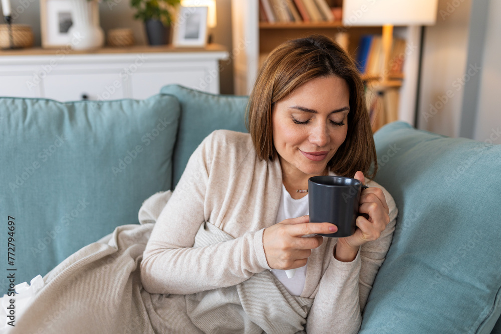 Young happy relaxed woman enjoying quiet moments at home with cup of tea or coffee, smiling female holding mug with hot drink resting on sofa in living room and dreaming, relaxing of everything Young happy relaxed woman enjoying quiet moments at home with cup of tea or coffee, smiling female holding mug with hot drink resting on sofa in living room and dreaming, relaxing of everything