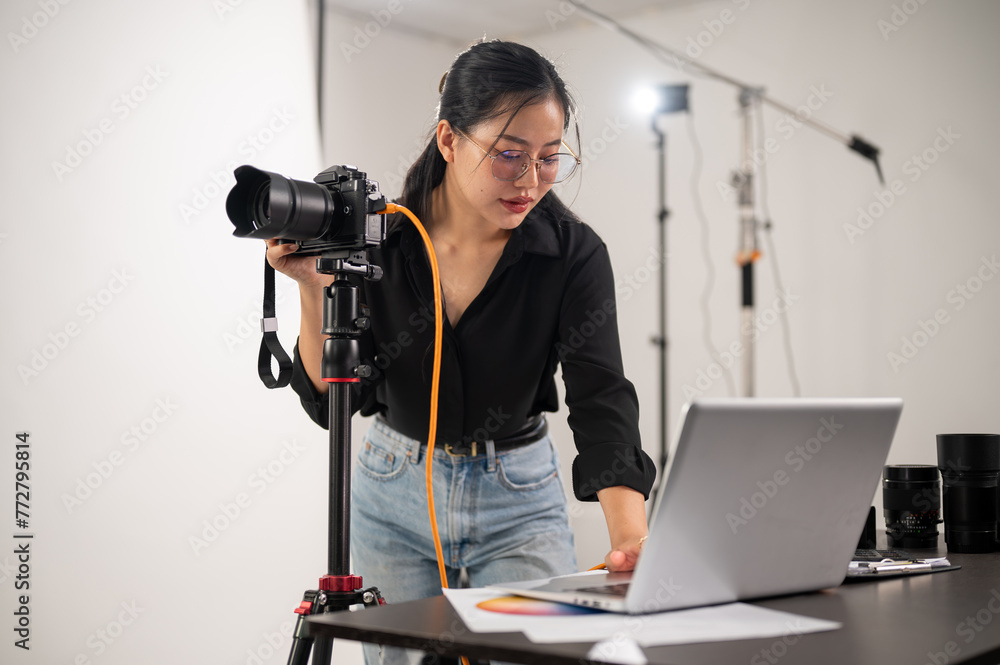 Cool, professional Asian female photographer is checking images on her laptop, working in the studio Cool, professional Asian female photographer is checking images on her laptop, working in the studio