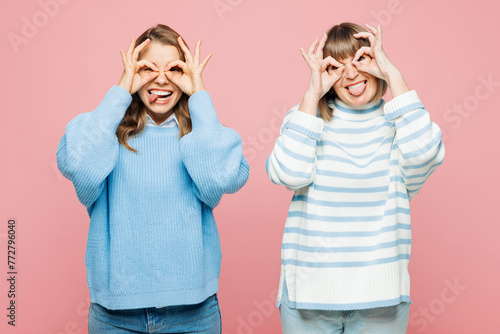 Elder parent mom 50s years old with young adult daughter two women together wear blue casual clothes look camera hold hands near eyes pov glasses isolated on plain pink background. Family day concept.