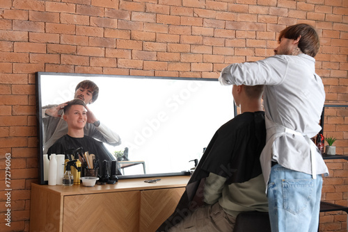 Male tattooed hairdresser cutting client's hair in barbershop