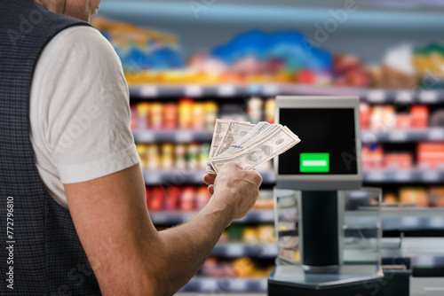 Automated self-service checkout at supermarket allows customers to pay for purchases with cash money. Instant payment: Cash dollars inserted into self-service terminal at the supermarket checkout