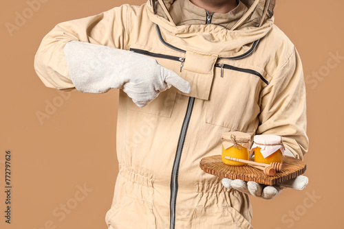 Male beekeeper pointing at honey on brown background, closeup photo