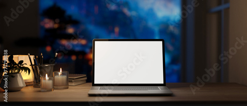 Home workspace at night features a white-screen laptop computer mockup on a wooden desk.