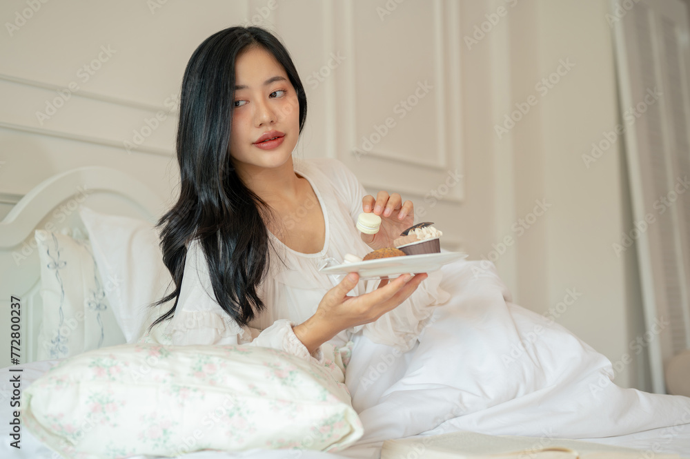 An attractive Asian woman in long dress pajamas is having breakfast in bed. An attractive Asian woman in long dress pajamas is having breakfast in bed.