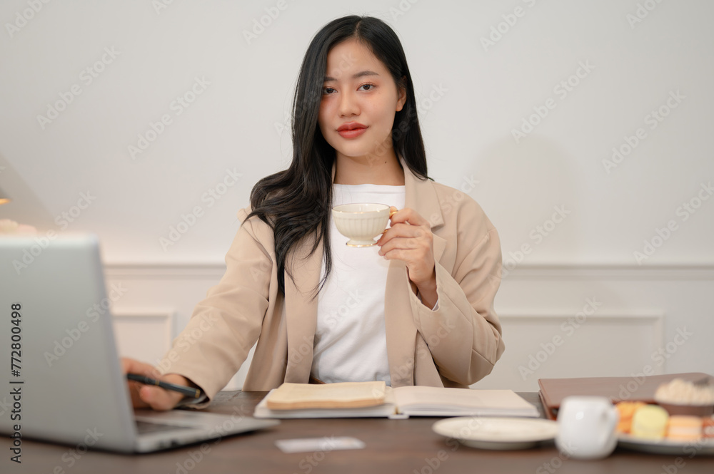 An elegant Asian businesswoman is sipping coffee while working at her desk in her office. An elegant Asian businesswoman is sipping coffee while working at her desk in her office.