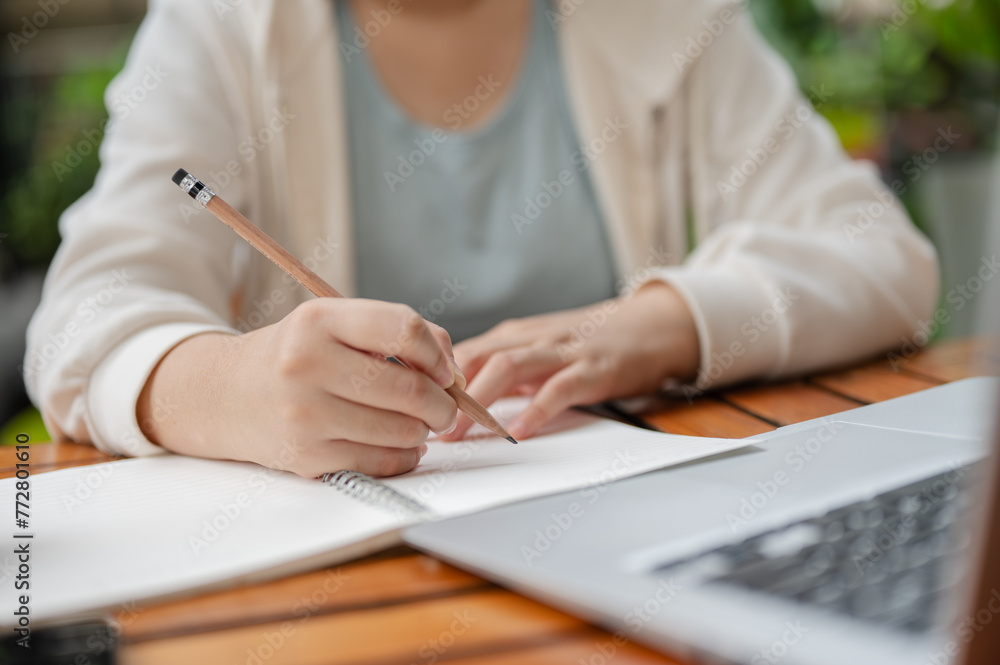 A woman is writing or taking notes in the notebook while working remotely at an outdoor space. A woman is writing or taking notes in the notebook while working remotely at an outdoor space.