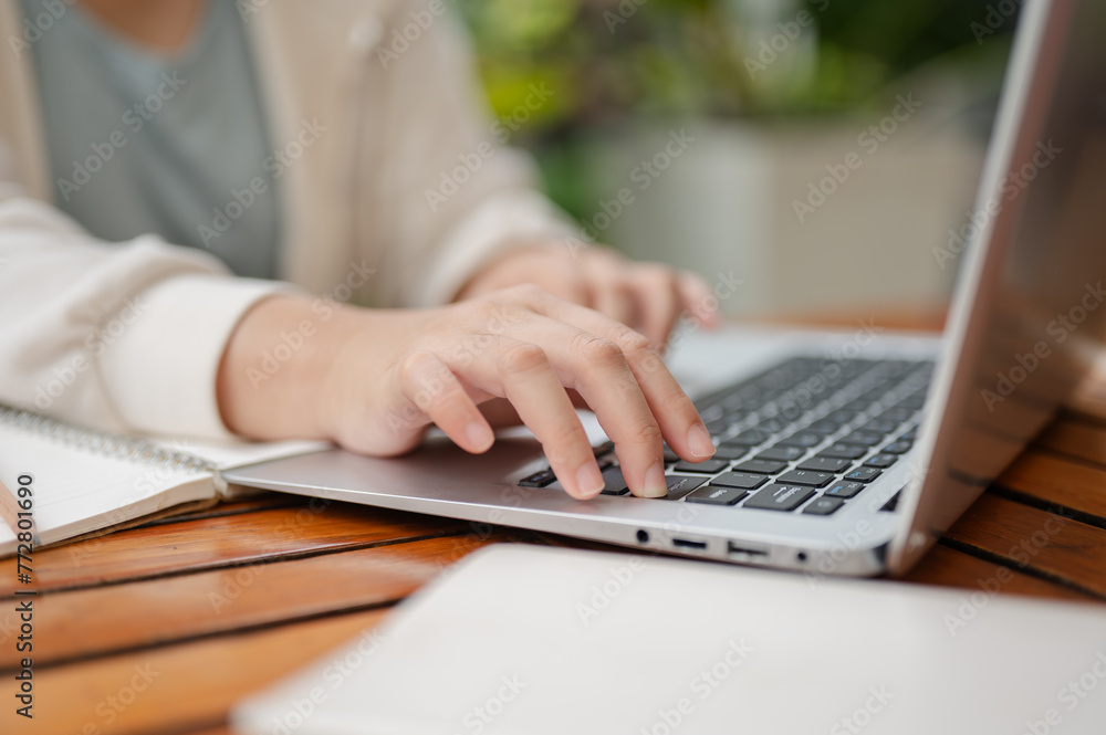 A cropped image of a woman is working remotely at an outdoor space, typing on laptop keyboard. A cropped image of a woman is working remotely at an outdoor space, typing on laptop keyboard.