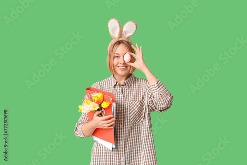 Happy adult female secretary in bunny ears with documents folder, tulips and egg on green background. Easter celebration