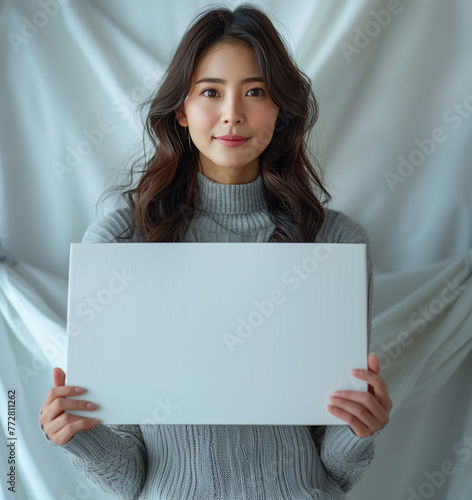 full body of beautiful asian woman presenting a product, the blank white box and looking forward to the camera. In the background is white color backdrop.
