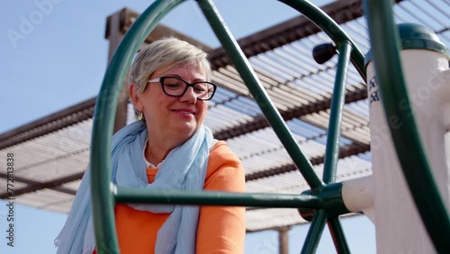Closeup of mature woman using public adapted fitness machine. Exercising on elderly age concept.