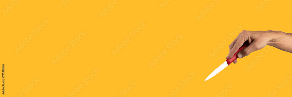 Black male hand holding a red cooking knife isolated on yellow banner Black male hand holding a red cooking knife isolated on yellow banner