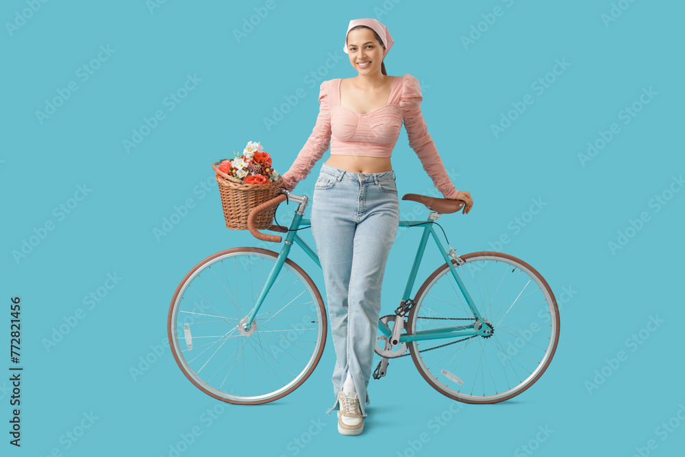 Beautiful young woman with bicycle and bouquet of flowers on blue background - obrazy, fototapety, plakaty 