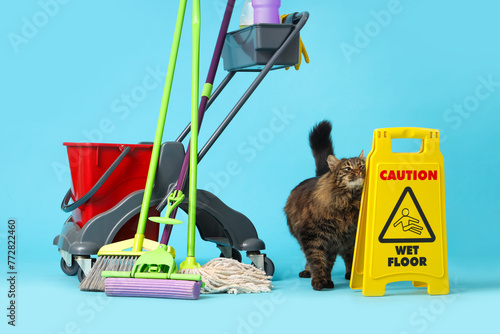 Cute cat with trolley of cleaning supplies on blue background