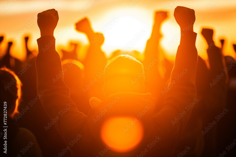 mass with raised fists backlit at sunset