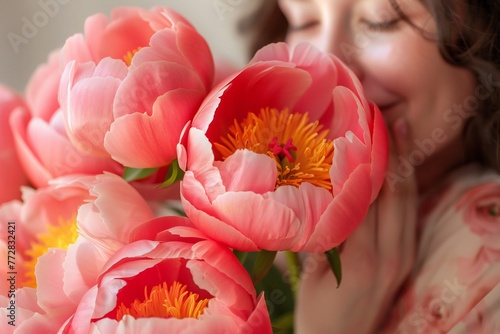 Fototapeta Naklejka Na Ścianę i Meble -  Happy woman smelling a bouquet of coral sunset peony.