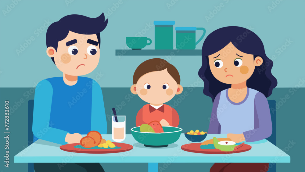 An image of two siblings sitting together at the dinner table but the older one is staring dejectedly at their plate as the parents are focused An image of two siblings sitting together at the dinner table but the older one is staring dejectedly at their plate as the parents are focused
