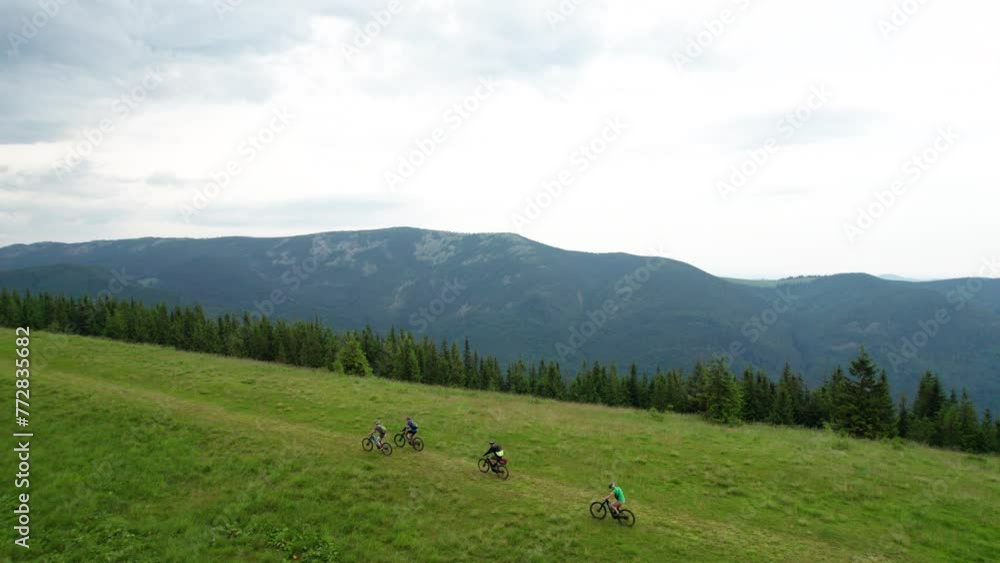 Group of cyclists men riding electric bikes outdoors. Aerial view of male tourists biking on grassy trail in the mountains at summer. Concept of sport, active leisure and nature. Group of cyclists men riding electric bikes outdoors. Aerial view of male tourists biking on grassy trail in the mountains at summer. Concept of sport, active leisure and nature.