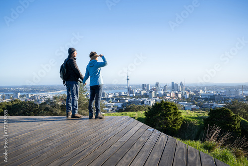 Couple standing on boardwalk at Mt Eden summit. Sky Tower and Auckland Harbour Bridge in the distance. Auckland. photo