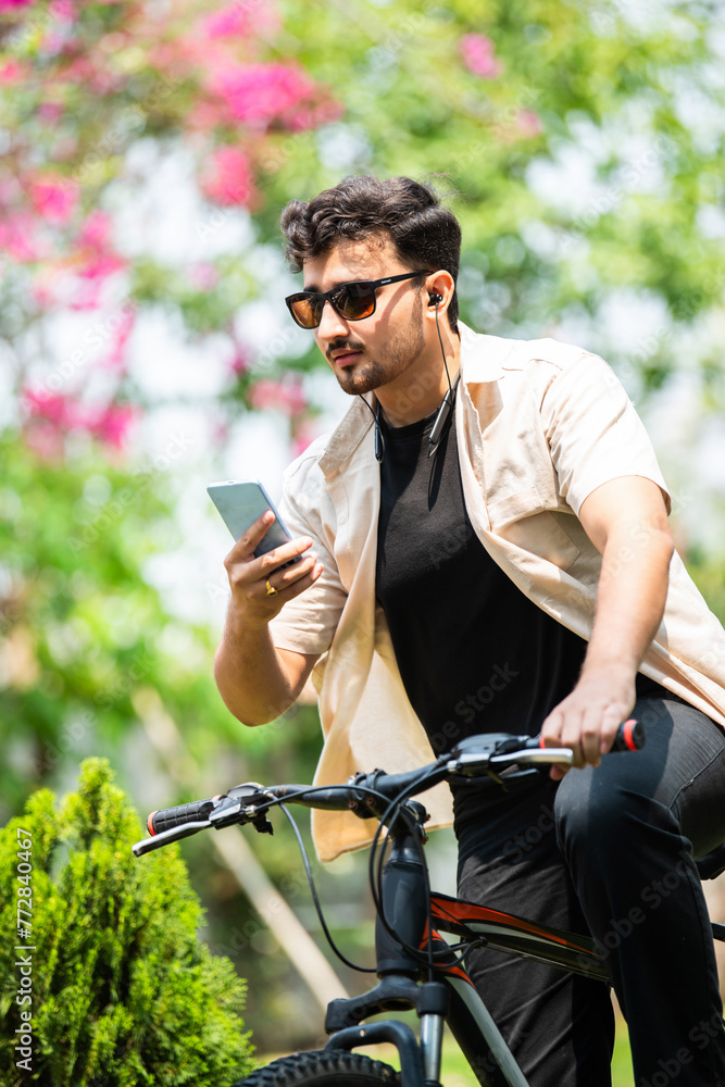 Indian good looking young man rides bicycle and stops for using smartphone Indian good looking young man rides bicycle and stops for using smartphone