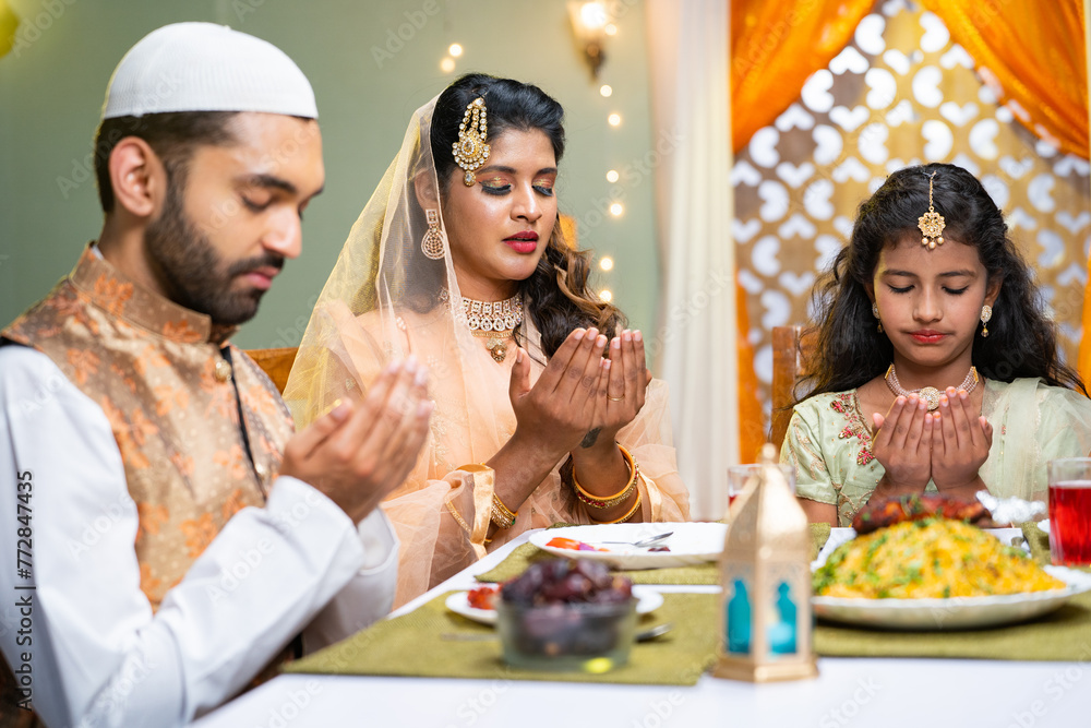 Indian Muslim family with kid praying at ramadan iftar dinner before eating at home - concept of traditional festival culture, rmzan kareem and family bonding - obrazy, fototapety, plakaty 